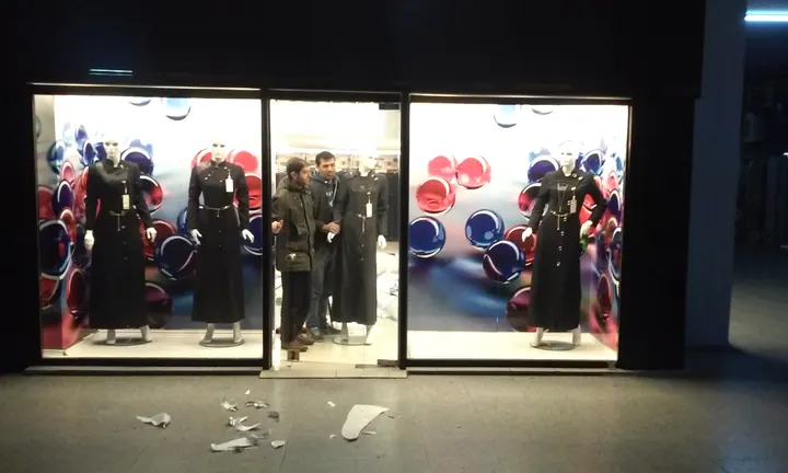 Mağaza vitrini dekoratif baskısı — Mankenlerin arkasındaki renkli kampanya görsellerinin gece görünümü.